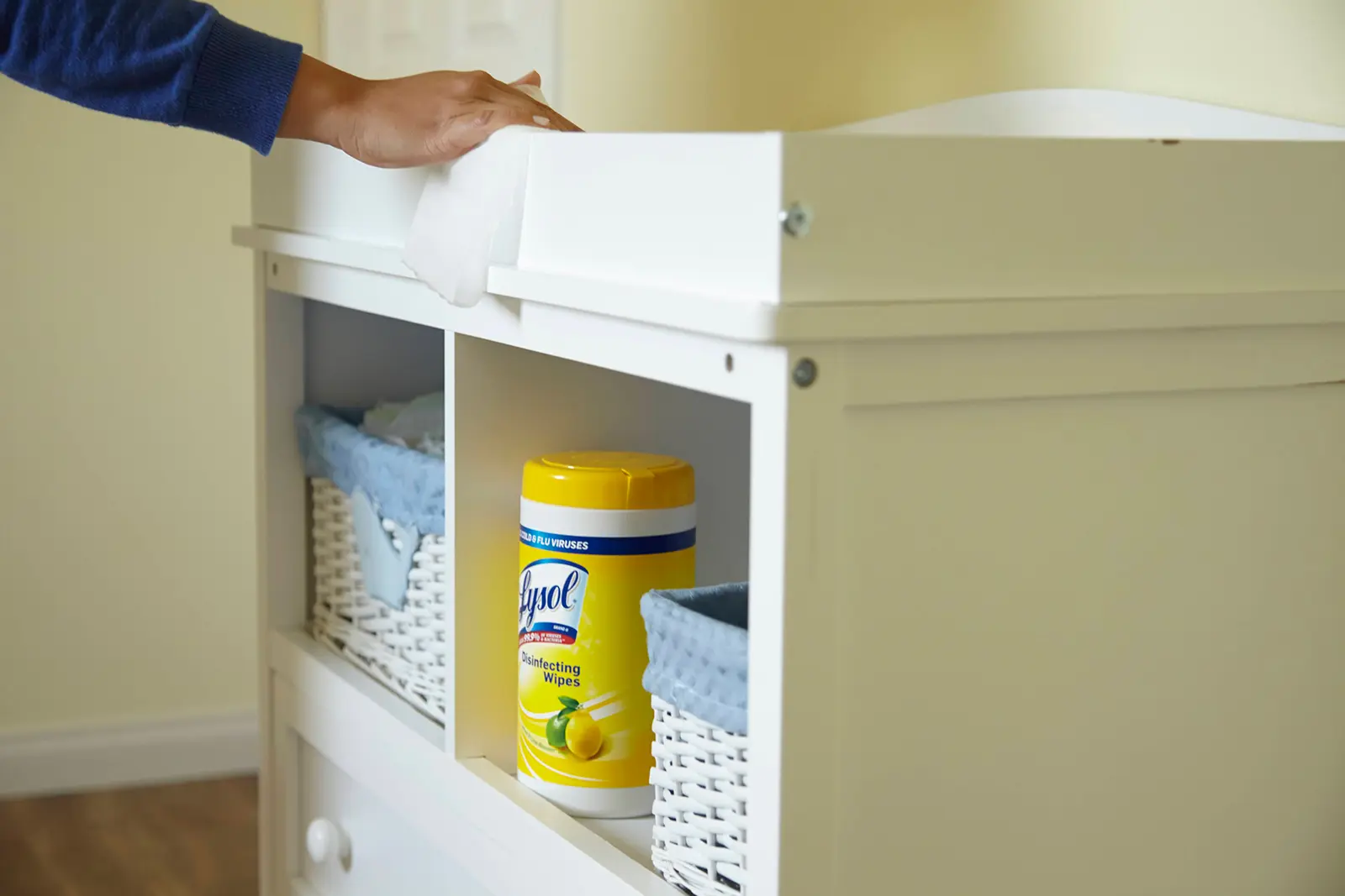 Person wiping cabinet with baskets and canister of Lysol Disinfecting Wipes on shelf