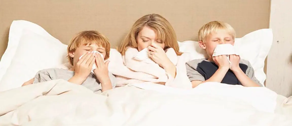 Family in bed looking ill with tissues to their noses