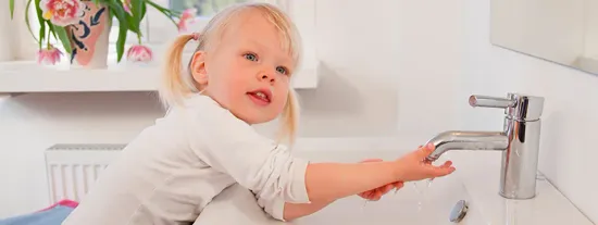 Young child leaning over bathroom sink next to block of soap