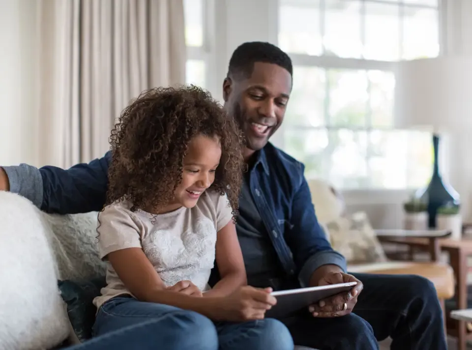 Parent and child sit smiling at tablet screen
